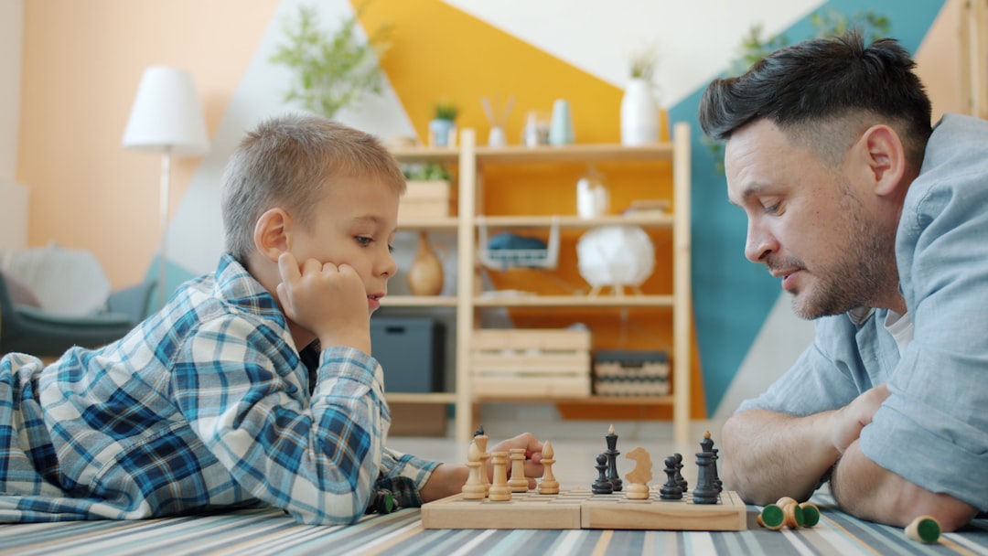 Father and child playing a strategy board game together on the floor, learning through play during school holidays