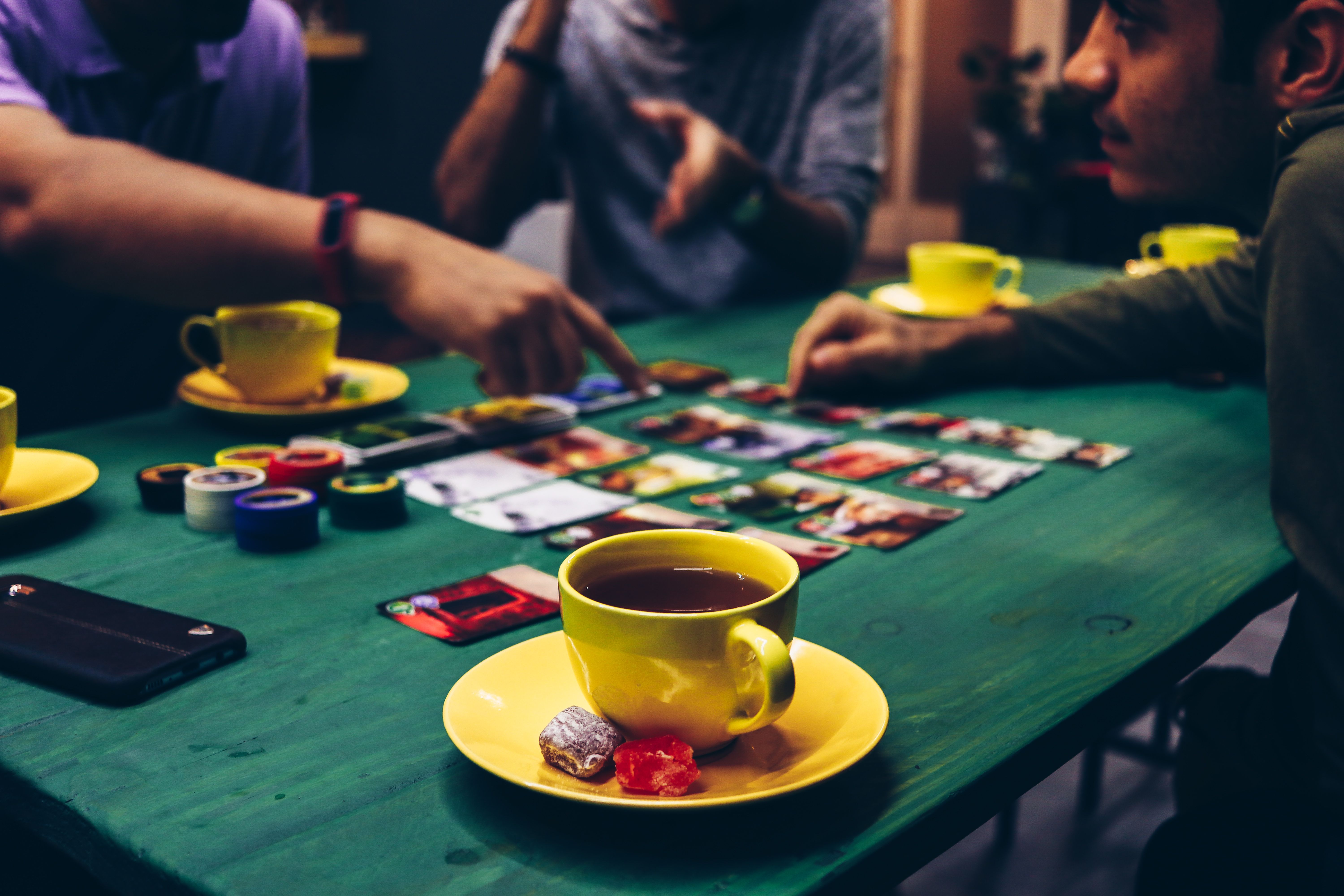 Group of friends playing a board game together with tea and snacks around a table