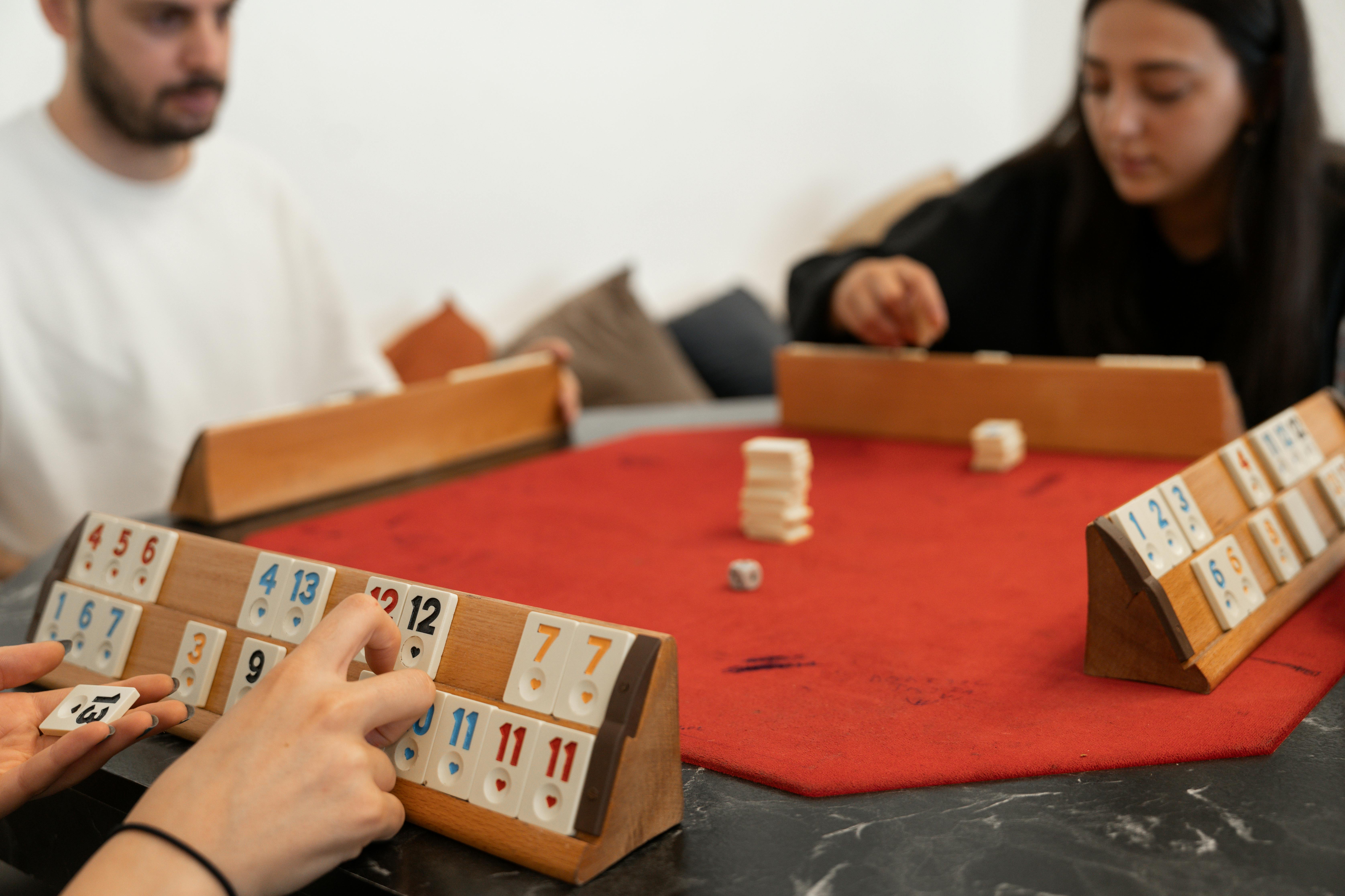 A group of adults gathered around a table playing a modern tabletop game, with colourful board game components spread across the table