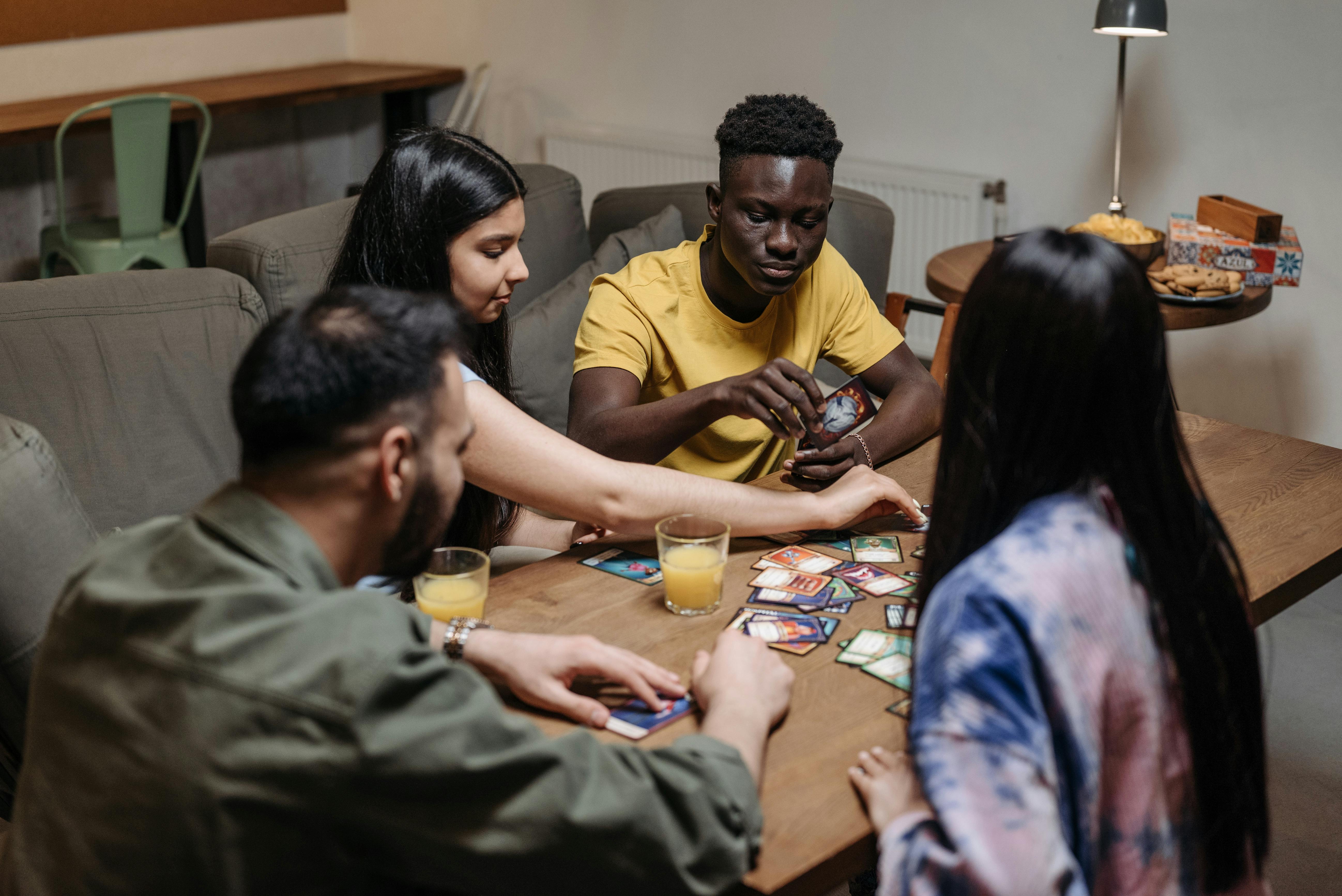 Adults playing an educational strategy board game around a wooden table with notepads and strategy cards visible